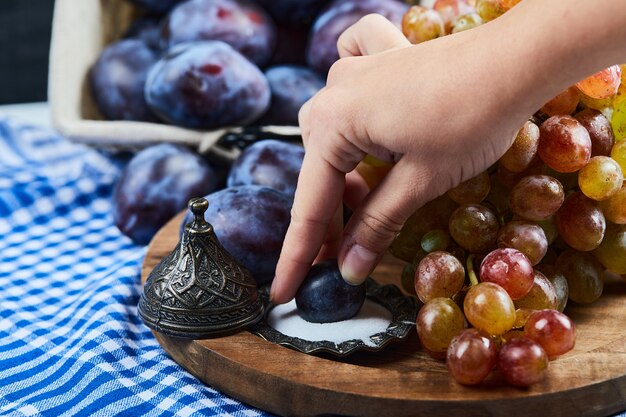 Ciruelas frescas, un racimo de uvas y sal sobre tabla de madera.