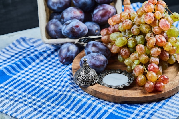 Ciruelas frescas y un racimo de uvas sobre mantel.