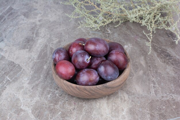 Ciruelas frescas en un tazón de madera sobre fondo de piedra.