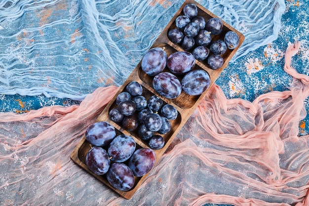 Foto gratuita ciruelas de jardín en bandeja de madera y en azul con manteles.