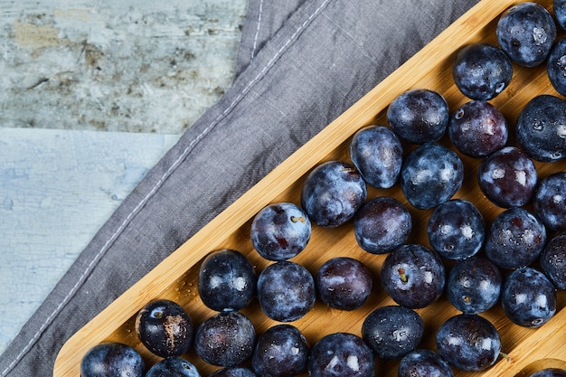 Foto gratuita ciruelas de jardín en bandeja de madera con mantel gris.