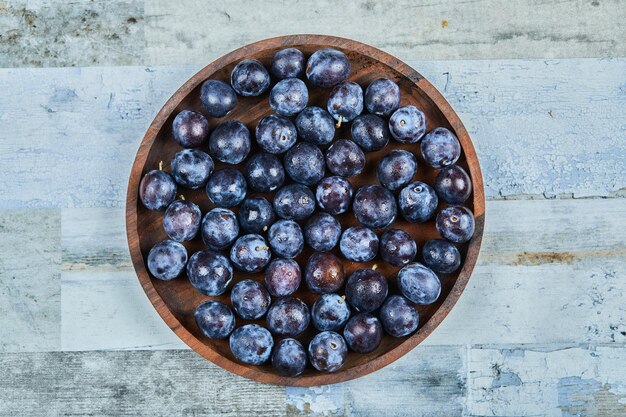 Ciruelas de jardín en un plato sobre un fondo azul. Foto de alta calidad