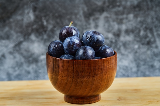 Ciruelas de jardín en un recipiente sobre la mesa de madera.