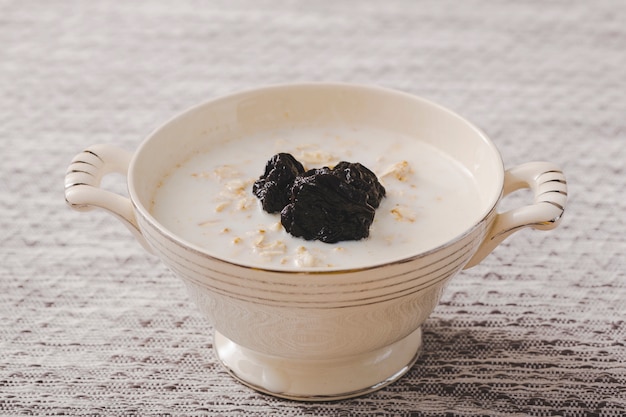 Ciruelas negras secas en el desayuno de avena sobre el mantel individual