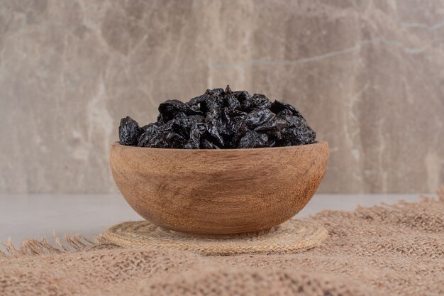 Ciruelas negras secas en una taza de madera sobre un trozo de arpillera.