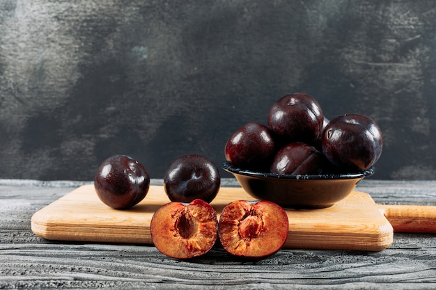 Foto gratuita ciruelas saladas en un plato y tablero de madera sobre una madera blanca y fondo gris oscuro. vista lateral.