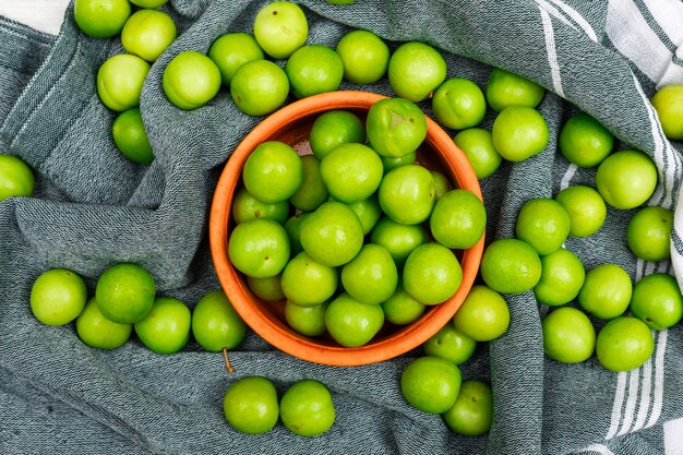 Ciruelas verdes carnosas en un tazón naranja cerca de toalla de cocina