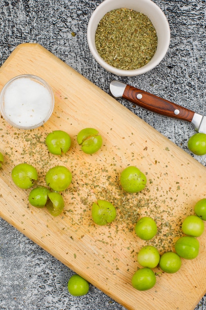 Foto gratuita ciruelas verdes picantes con una pequeña barra de sal, tomillo seco y un cuchillo de frutas en una tabla de cortar en la superficie gris del grunge, primer plano.