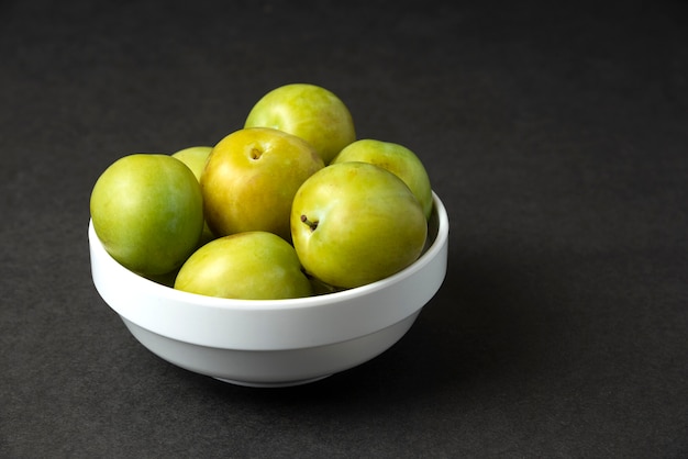 Ciruelas verdes en un platillo de cerámica blanca