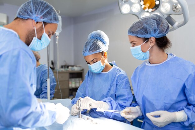Cirugía urgente Cirujanos inteligentes inteligentes profesionales parados cerca del paciente y realizando una operación mientras le salvan la vida
