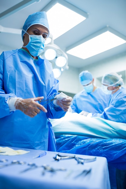 Cirujano celebración herramienta quirúrgica mientras que los colegas que realizan la operación