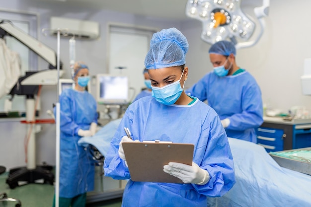 Foto gratuita cirujano escribiendo en el portapapeles en el anestesiólogo de la sala de operaciones escribiendo las actualizaciones