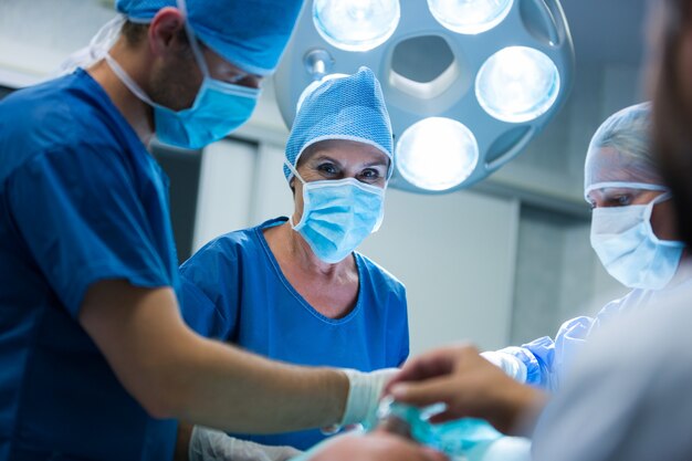 Cirujano que mira a la cámara mientras colega que realiza la operación en la sala de operación