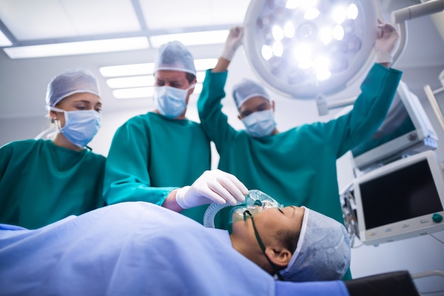 Cirujanos que ajustan la máscara de oxígeno en la boca del paciente en quirófano