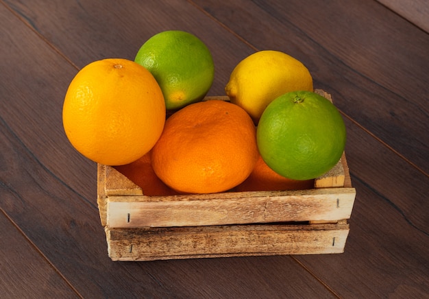 cítricos naranja mandarina limón verde y amarillo en caja de madera sobre marrón