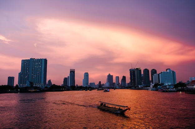Ciudad de río al atardecer y ferry en fondo de Bangkok
