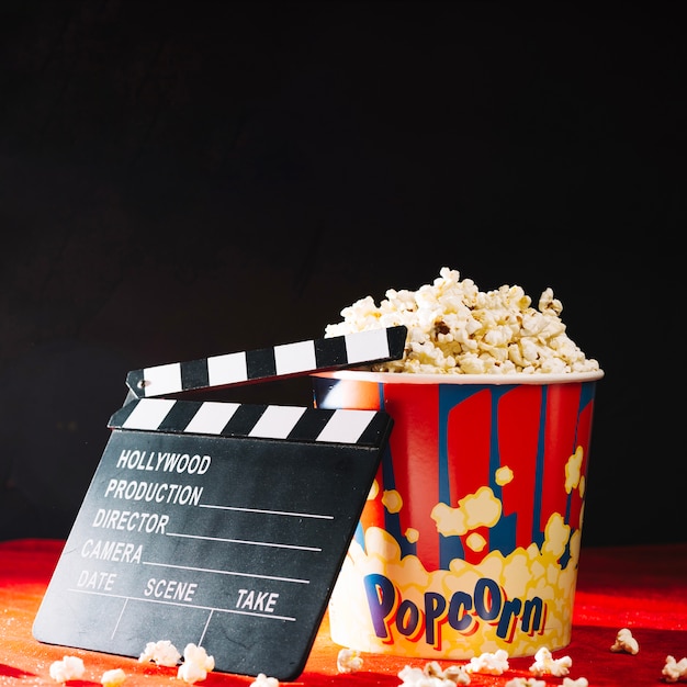 Foto gratuita clapperboard abierto apoyado contra el cubo de palomitas de maíz