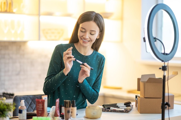 Clase de belleza en línea. Mujer joven en vestido verde mostrando consejos de maquillaje en línea