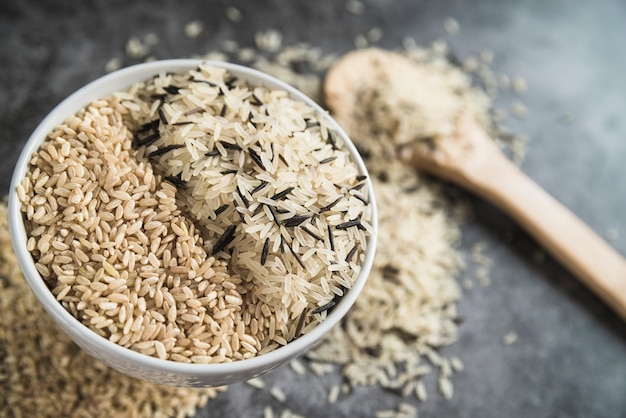 Clases de arroz en un tazón cerca de una cuchara de madera