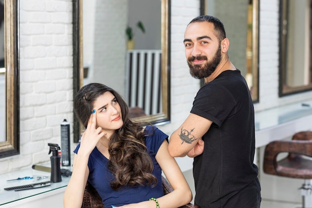 Una clienta enojada sentada en una silla y mirando a su barbero Foto de alta calidad
