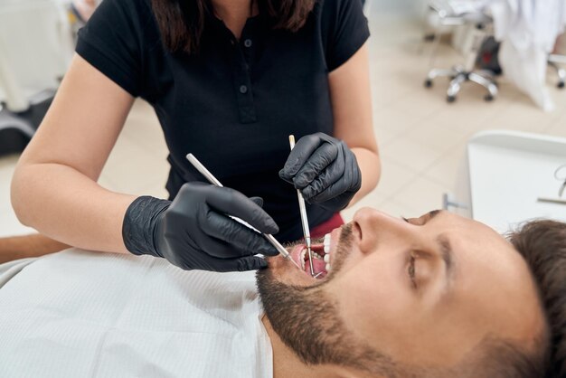 Cliente acostado con la boca abierta mientras el médico cura los dientes