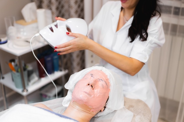 El cliente se acuesta en el salón en la mesa de cosmetología con una máscara blanca en el rostro.