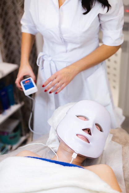 El cliente se acuesta en el salón en la mesa de cosmetología con una máscara blanca en el rostro.