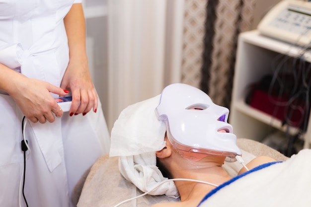 El cliente se acuesta en el salón en la mesa de cosmetología con una máscara blanca en el rostro.