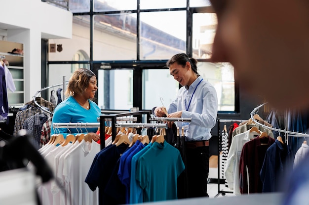 Foto gratuita cliente adicto a las compras mirando la nueva colección de moda, discutiendo material de ropa en una tienda de ropa. mujer afroamericana comprando ropa formal, revisando estantes con artículos elegantes