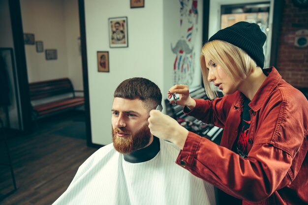 Cliente durante el afeitado de barba en peluquería. Peluquería femenina en el salón. Igualdad de género. Mujer en la profesión masculina.