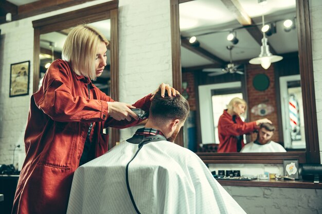 Cliente durante el afeitado de barba en peluquería. Peluquería femenina en el salón. Igualdad de género. Mujer en la profesión masculina.