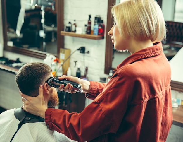 Cliente durante el afeitado de la barba en la peluquería. Peluquería femenina en el salón. Igualdad de género. Mujer en la profesión masculina.