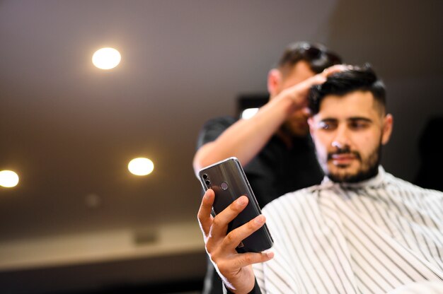 Cliente de ángulo bajo en peluquería mirando el teléfono con espacio de copia