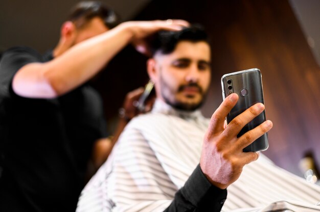 Cliente de ángulo bajo en peluquería mirando el teléfono