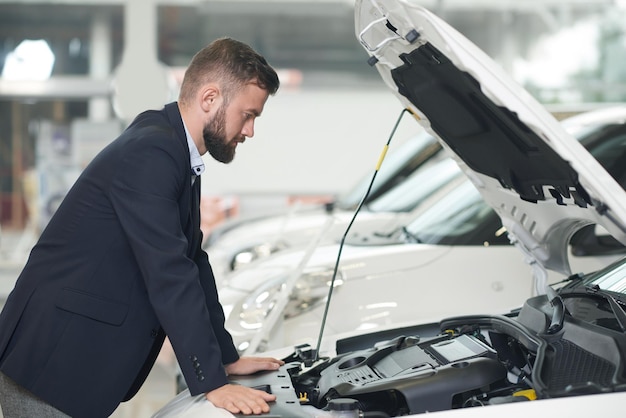 Cliente del centro de automóviles mirando debajo del capó del automóvil