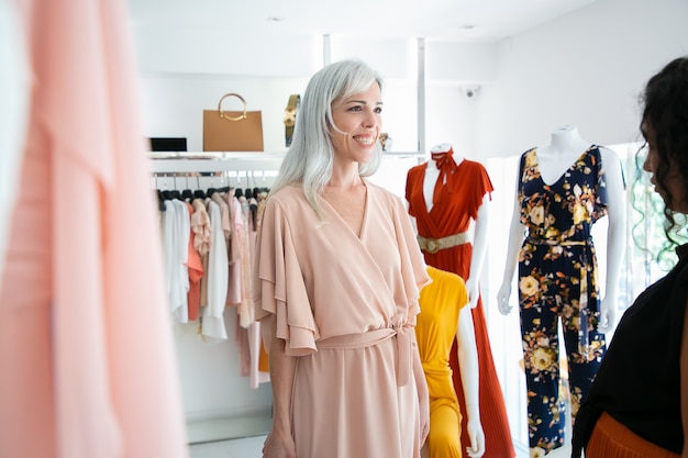 Cliente feliz probándose un vestido nuevo en boutique. Mujer eligiendo ropa en tienda de moda. Comprar ropa en concepto boutique.