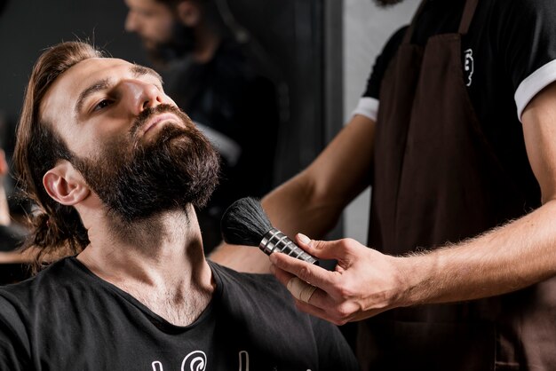 Cliente masculino con barba cerca de peluquería sosteniendo la brocha de afeitar