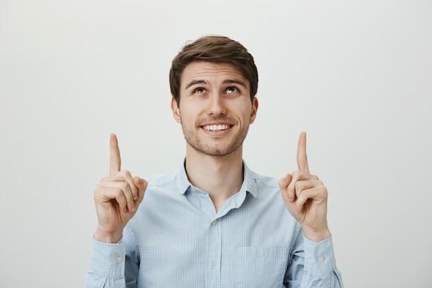 Cliente masculino complacido apuntando y mirando hacia arriba, sonriendo feliz