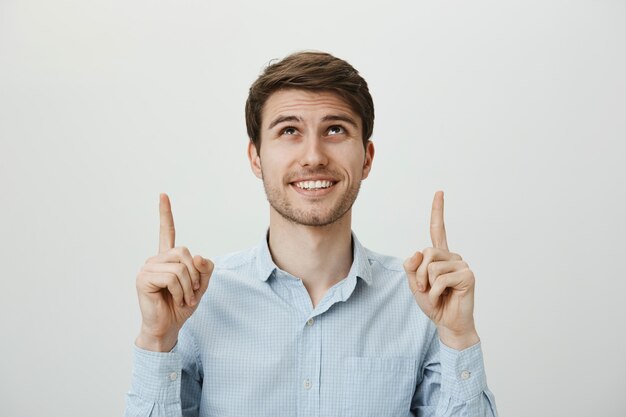 Cliente masculino complacido apuntando y mirando hacia arriba, sonriendo feliz