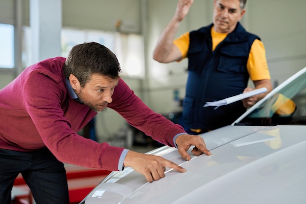 Cliente masculino examinando el capó del coche mientras está en el taller de reparación de automóviles