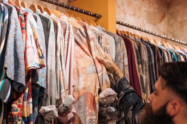 Cliente masculino que elige la camisa que cuelga en el carril en la tienda