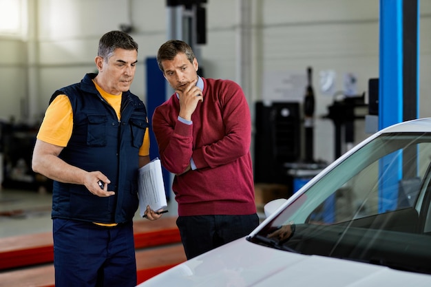 Cliente preocupado hablando con un mecánico de automóviles en un taller de reparación de automóviles