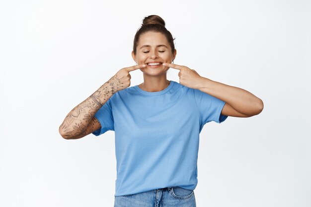 Cliente satisfecho de la clínica dental señalando con el dedo los dientes blancos. Mujer feliz mostrando sonrisa blanqueada en blanco