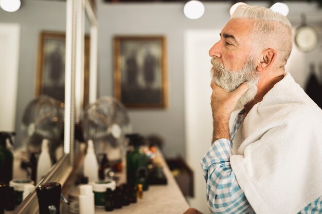 Cliente senior estimando trabajos de barbero en espejo.