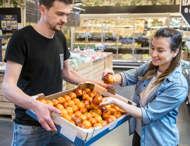 Clientes sonrientes que compran naranjas sicilianas en la sección de comestibles