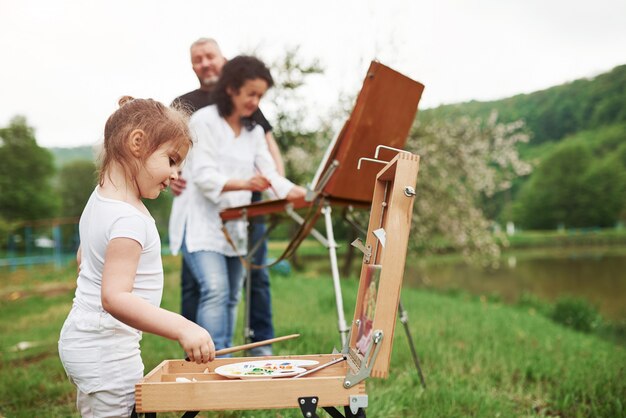 Clima nublado. La abuela y el abuelo se divierten al aire libre con su nieta. Concepción de la pintura