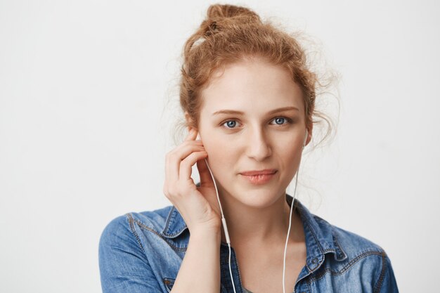 Close-ip retrato de amable hermosa joven pelirroja con ojos azules, usando auriculares mientras escucha música