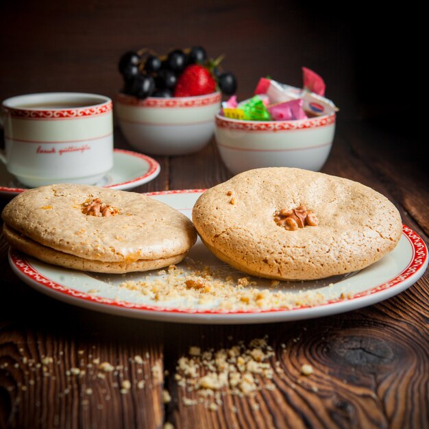 Close-up galletas caseras con una taza de té, dulces y bayas en la mesa de madera