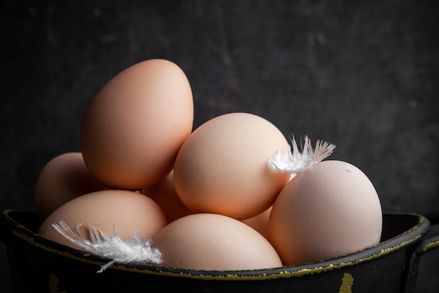 Close-up huevos en maceta con plumas sobre fondo de madera oscura. horizontal