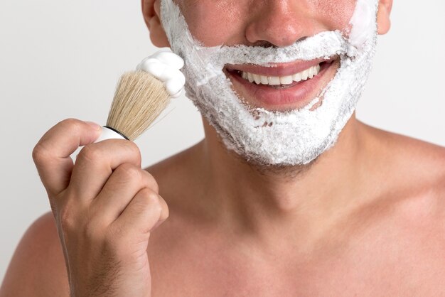 Close-up de joven aplicando espuma de afeitar con brocha en la cara